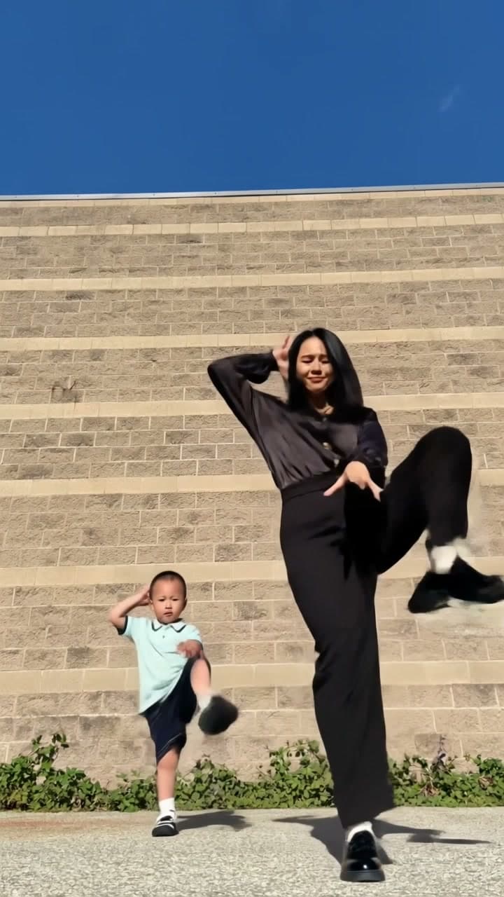 AI-generated woman in a dark blouse and a boy in a mint polo doing the two-person dance in front of a stone wall.